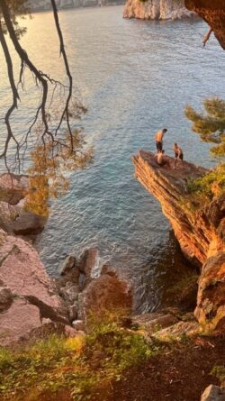 an image of people stood on cliffs over the sea at sunset 